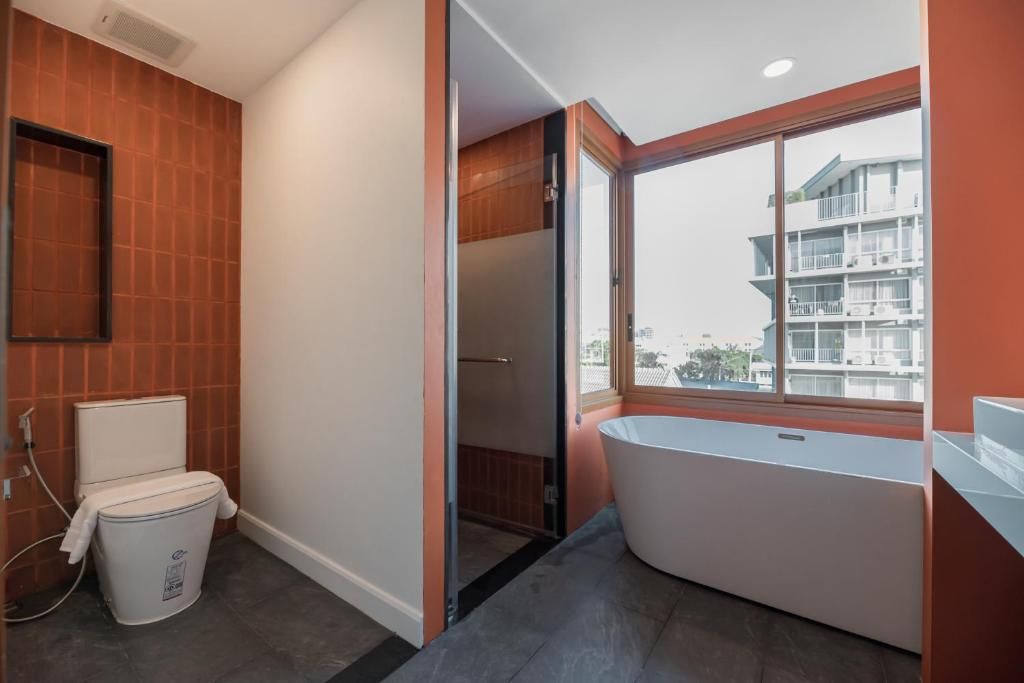 Un baño moderno con inodoro, bañera y ventana con vistas a un edificio.