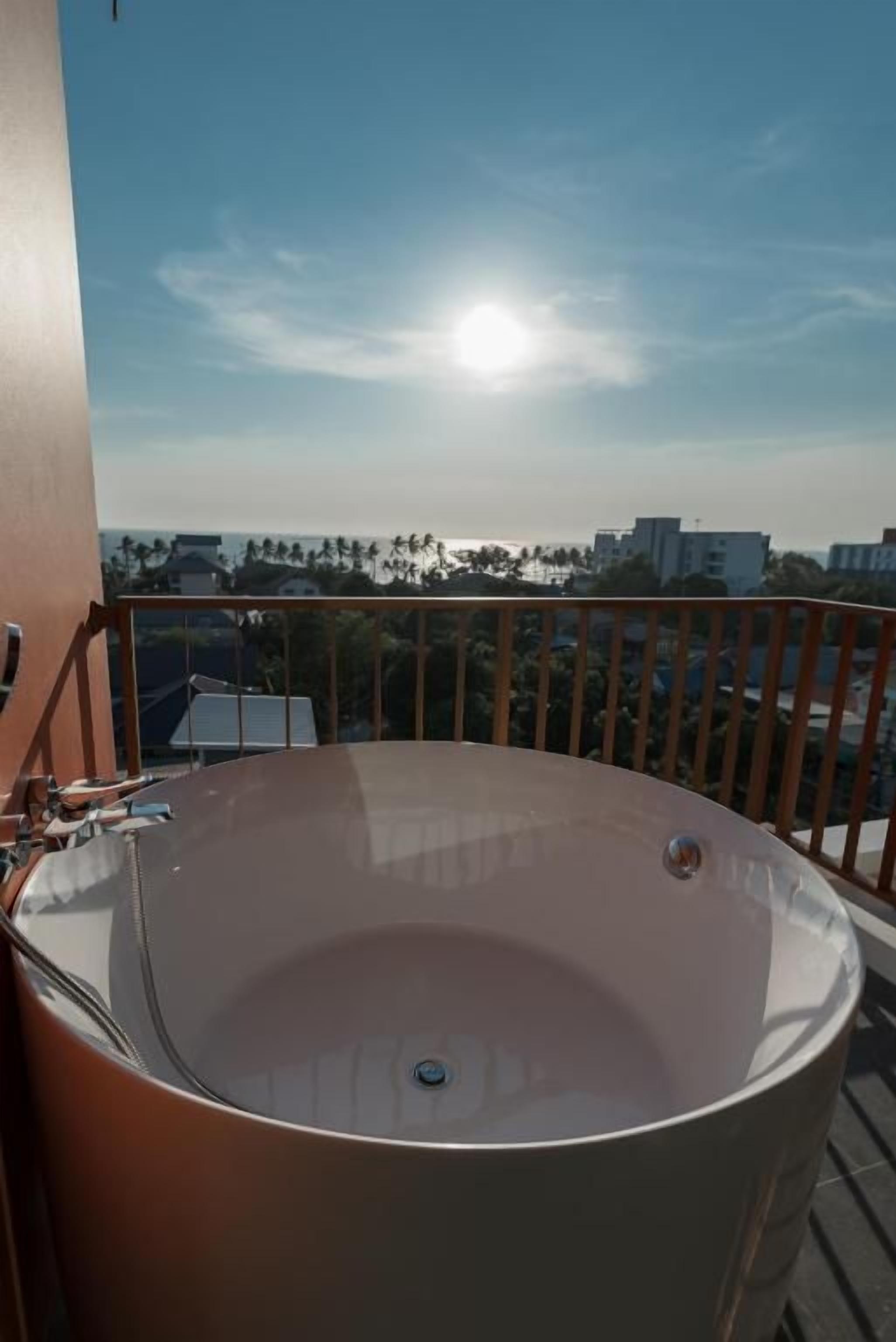 Una bañera grande y redonda en un balcón con vistas despejadas al paisaje urbano y palmeras al fondo.