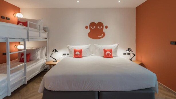 Une chambre d’hôtel avec un lit superposé, un grand lit et un luminaire fixé au mur.