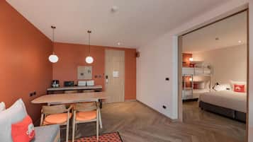 Una habitación de hotel moderna con zona de comedor, sofá, cama y un espacio independiente para dormir.