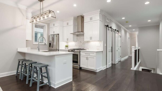 A modern kitchen with white cabinetry, a central island with bar stools, and built-in appliances. - Luxury Columbus Townhouse with Game Room & Patio (Columbus)