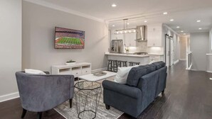 A modern living room with a gray sofa, a coffee table, and a TV on the wall. - Luxury Columbus Townhouse with Game Room & Patio (Columbus)