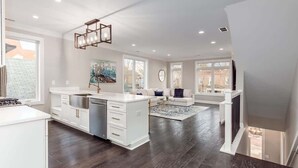 A spacious kitchen with white cabinetry, a central island, and a dining area with a large rug. - Luxury Modern Harrison West Home with Rooftop Terrace & Family Amenities (Columbus)