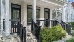 A two-story house with a front porch, black railings, and a small garden area. - Luxury Modern Harrison West Home with Rooftop Terrace & Family Amenities (Columbus)