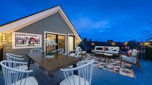A rooftop deck with a dining area, outdoor seating, and a framed sports photo. - Luxury Modern Harrison West Home with Rooftop Terrace & Family Amenities (Columbus)