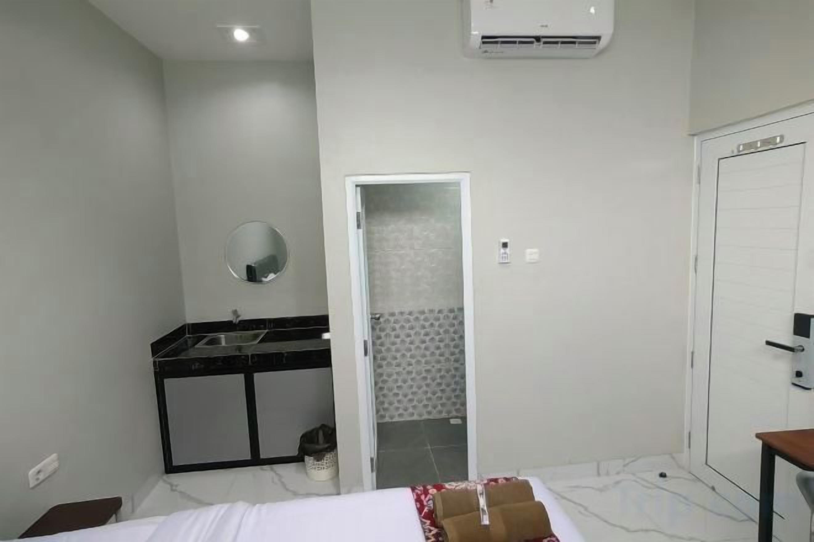 Une chambre d’hôtel avec un lit, un petit bureau, un miroir, un lavabo et une porte donnant sur une salle de bain.
