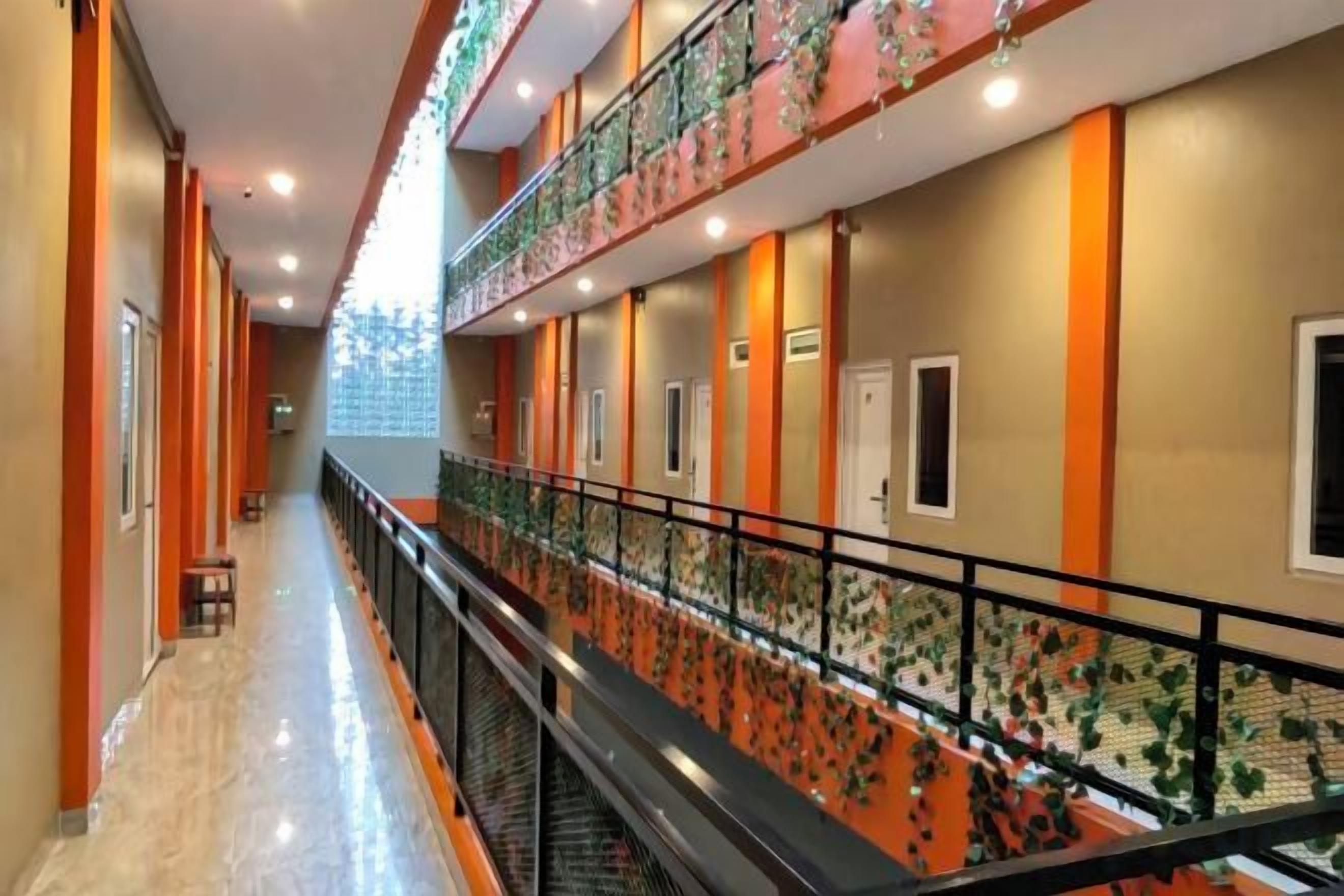 A hotel corridor with a central staircase, multiple doors, and a railing with a floral pattern.