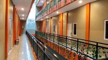 A hotel corridor with a central staircase, multiple doors, and a railing with a floral pattern.