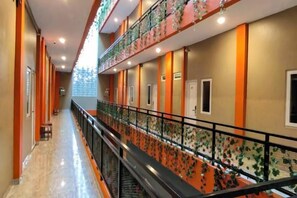 A hotel corridor with a central staircase, multiple doors, and a railing with a floral pattern. - Joy Hotel (Rajabasa)