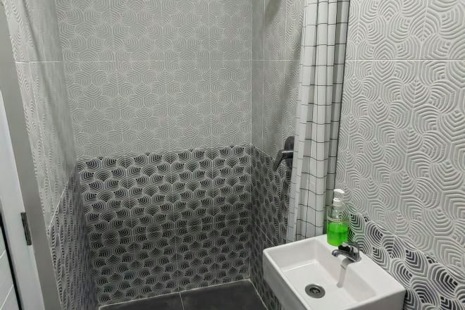 Ein Badezimmer mit gemusterten Fliesen, einem weißen Waschbecken und einer grünen Seifenflasche.