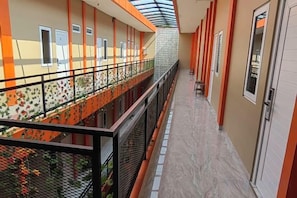 A corridor with a glass ceiling, a balcony with a railing, and a door with a sign. - Joy Hotel (Rajabasa)