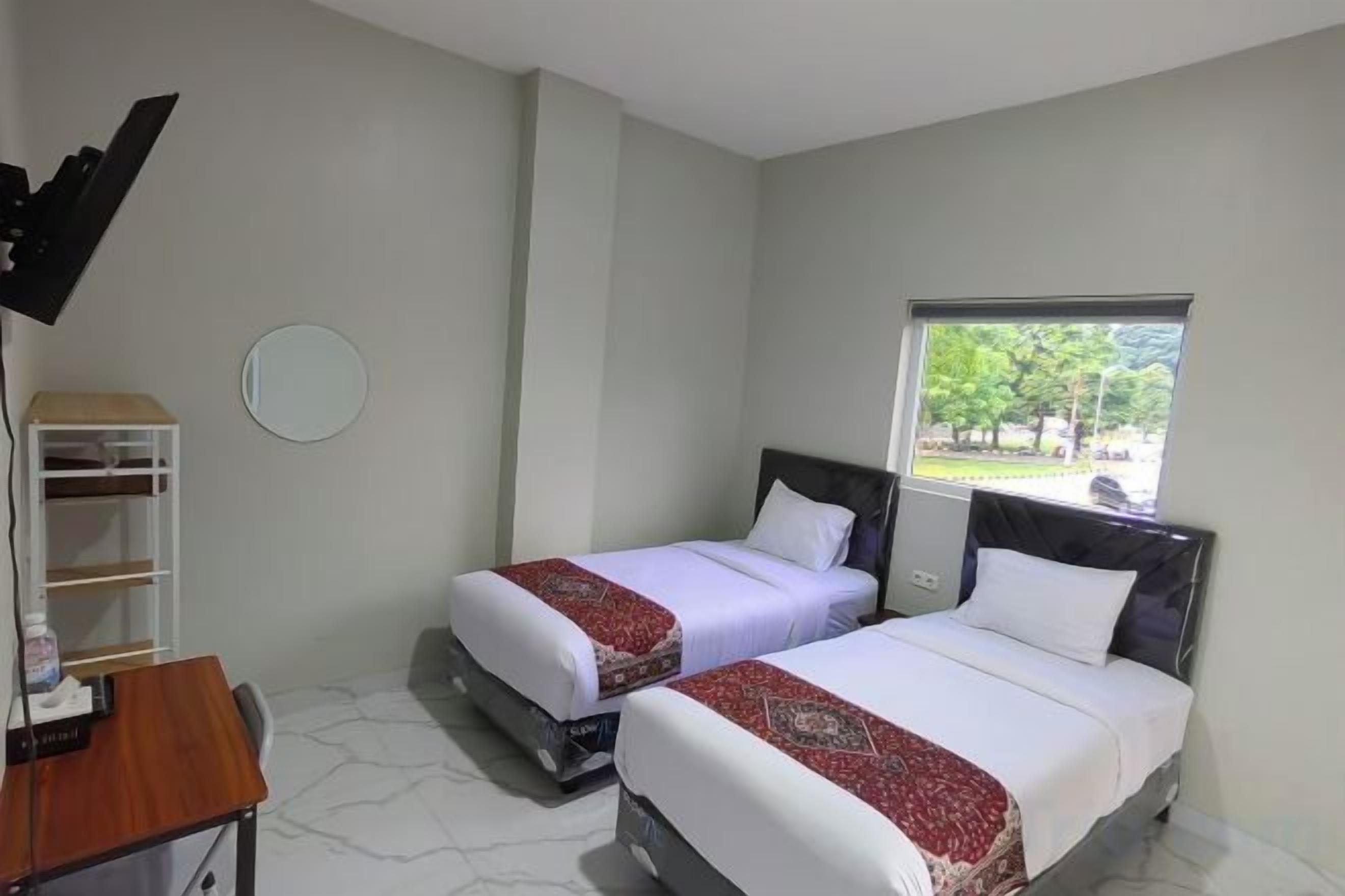 A hotel room with two beds, a desk, a chair, a mirror, and a window with a view of the outdoors.