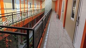 Un pasillo con piso de baldosas, paredes anaranjadas y barandilla de metal.