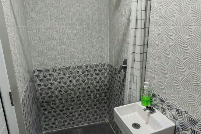 A bathroom with patterned walls, a shower, and a sink with a soap dispenser.