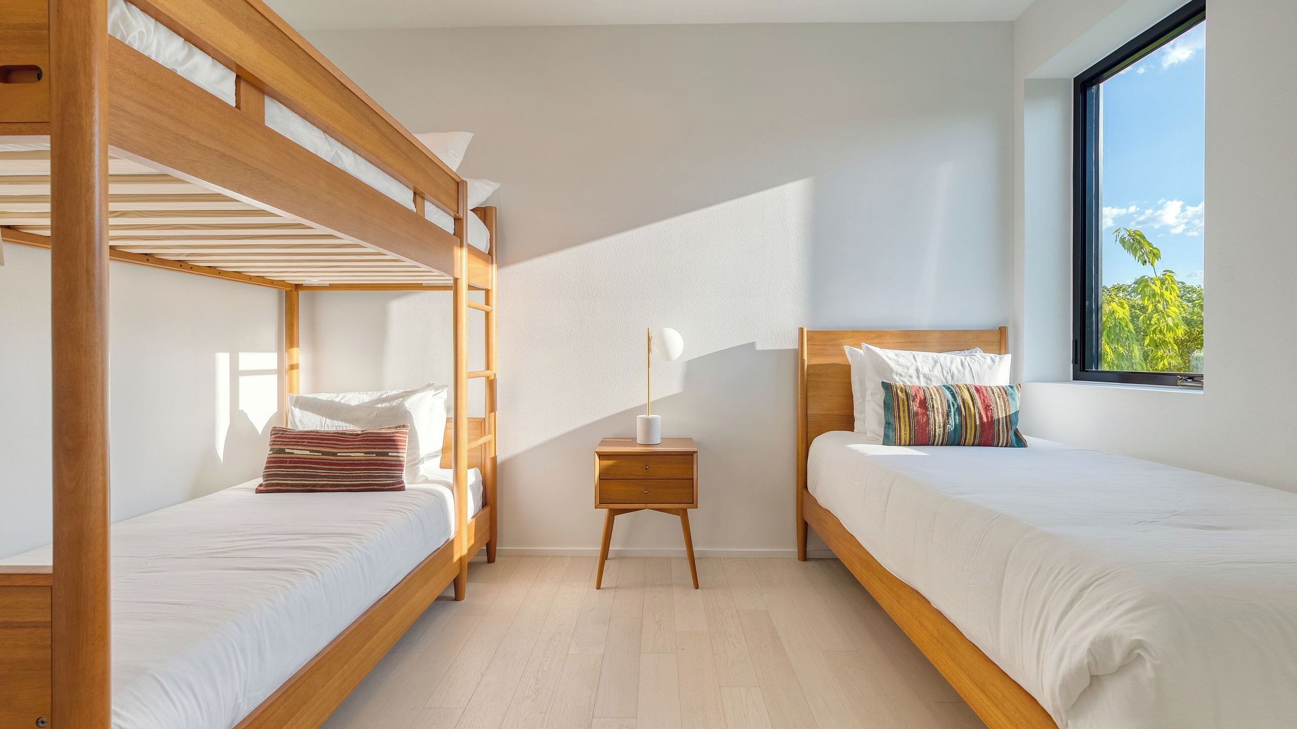 Une chambre avec deux lits superposés, une table de chevet avec une lampe et une fenêtre donnant sur des arbres.