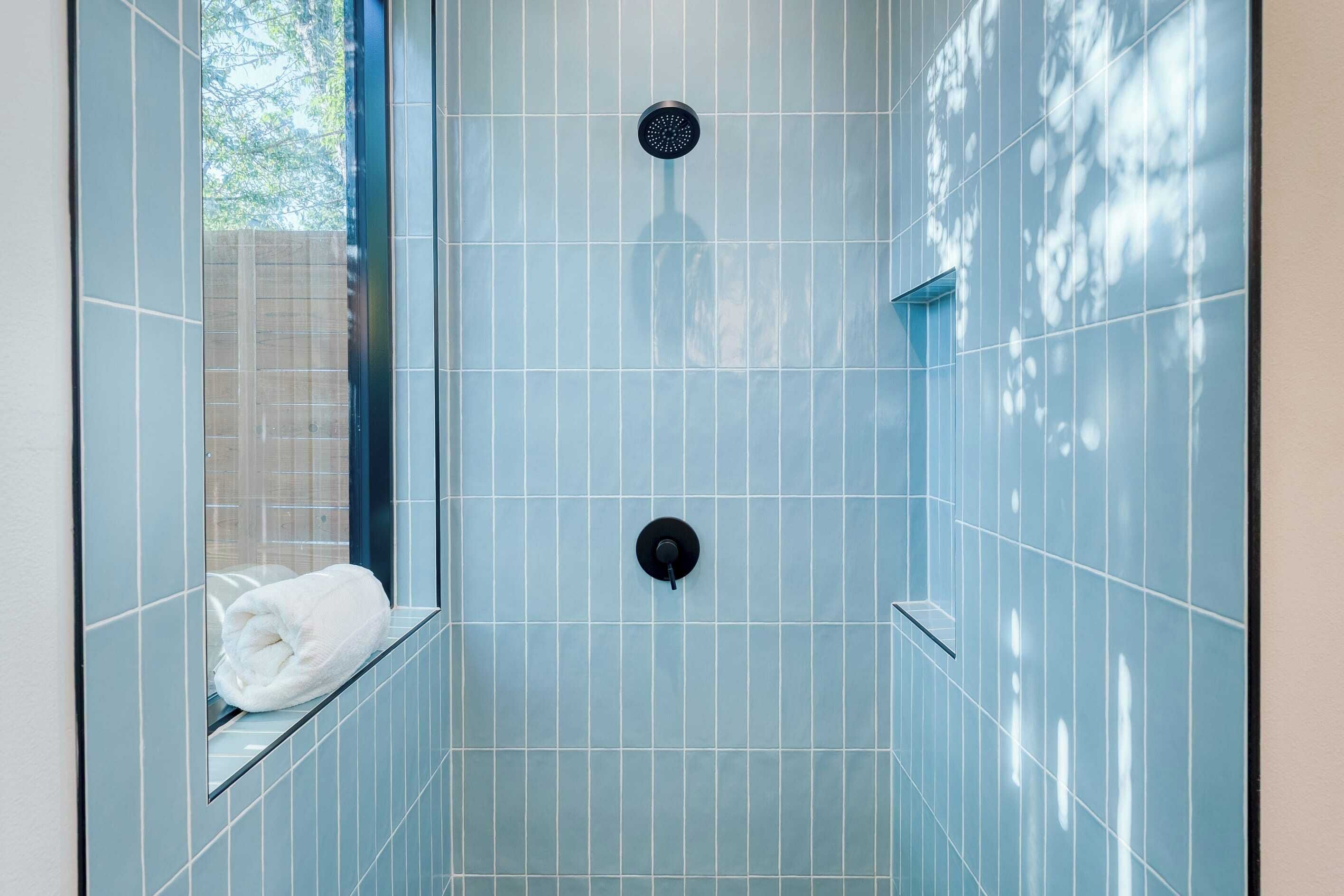 A shower with blue tiles, a towel, and a window.