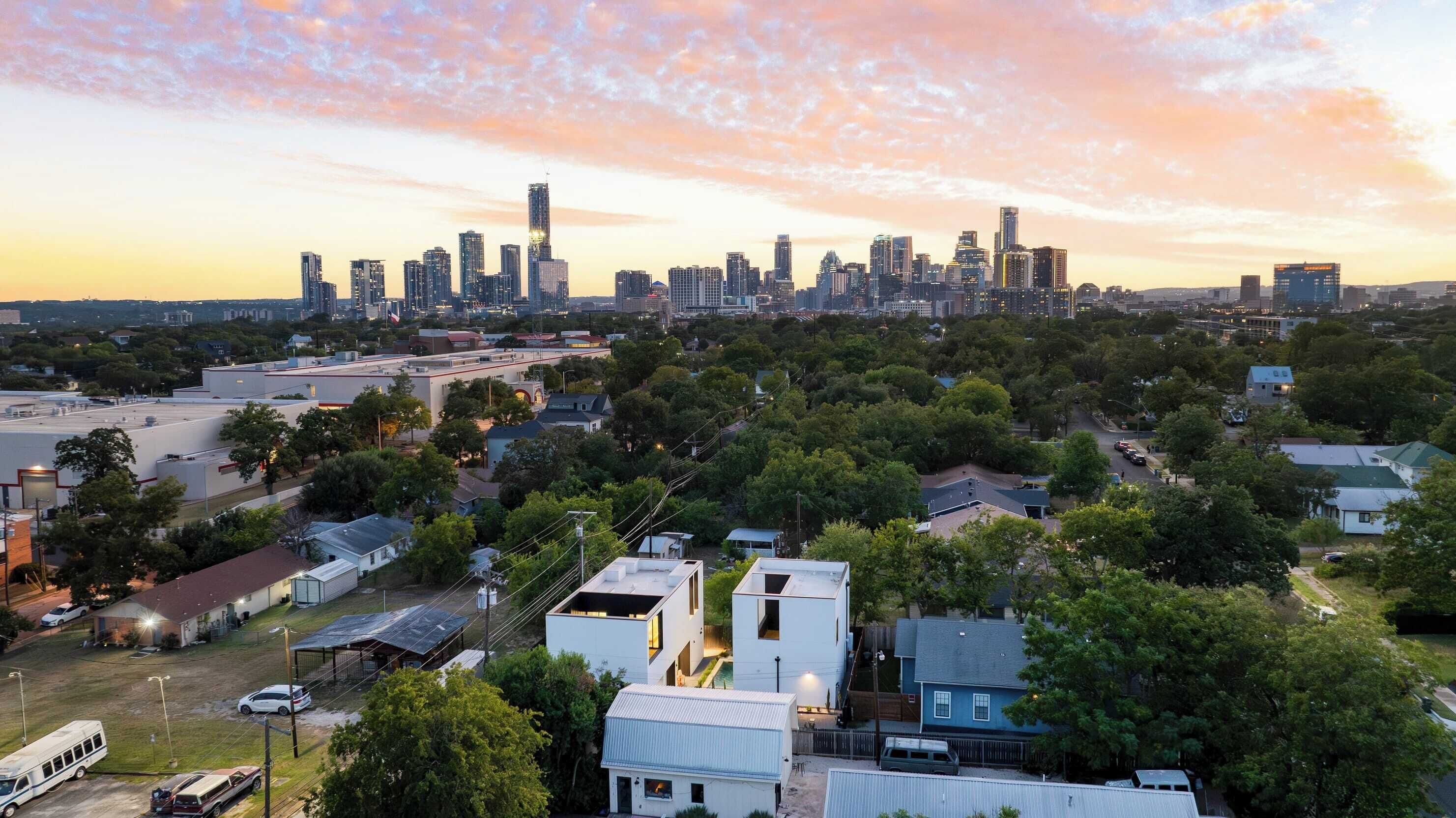 A residential area with modern houses, a parking lot, and a city skyline in the background.