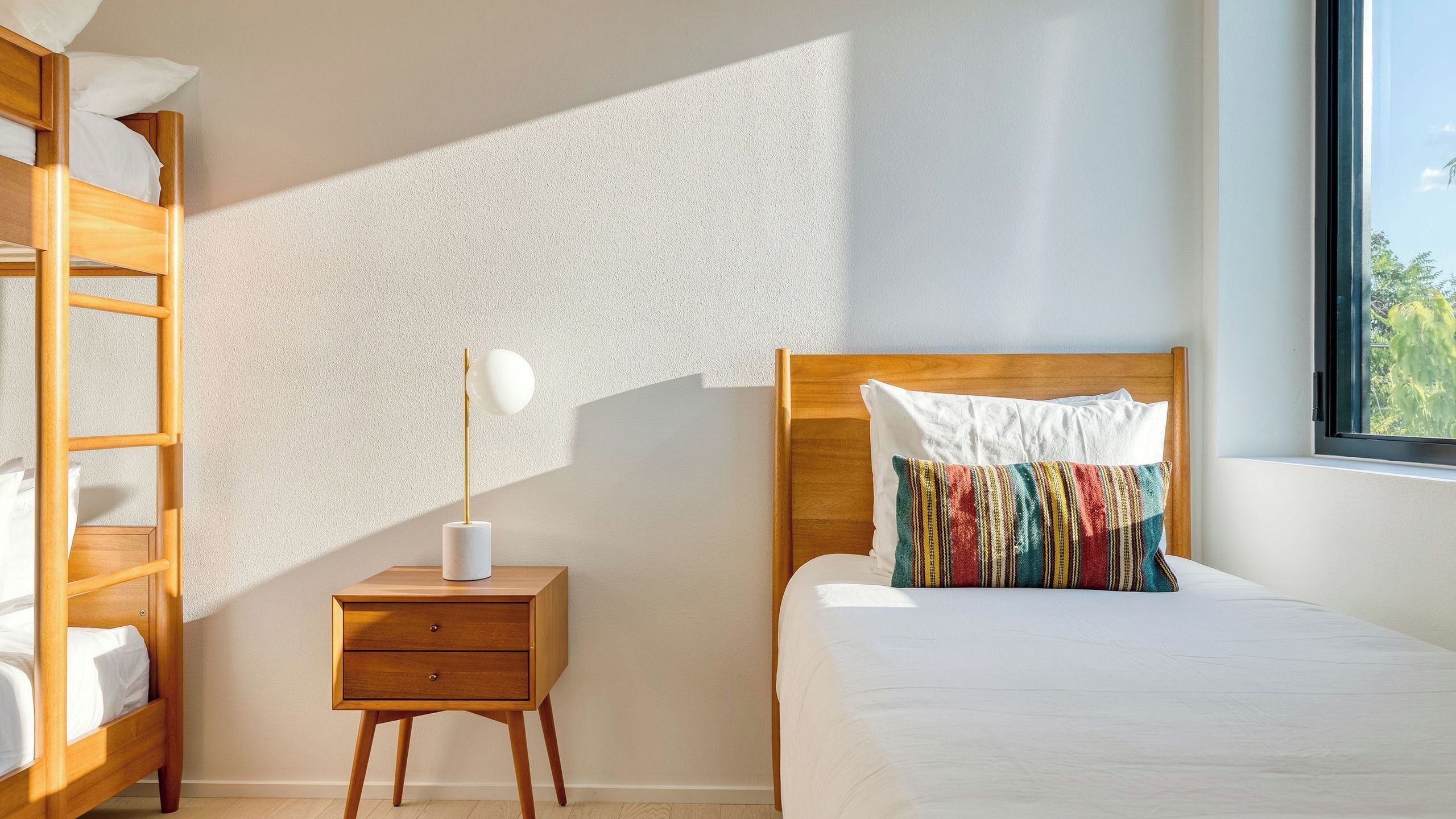 Un dormitorio con una cama, una mesita de noche con lámpara, una mesita auxiliar de madera y una ventana con vistas.