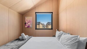 Ein modernes Schlafzimmer mit einem großen Bett, Blick auf Gebäude durch ein Fenster und einem Gemälde an der Wand.
