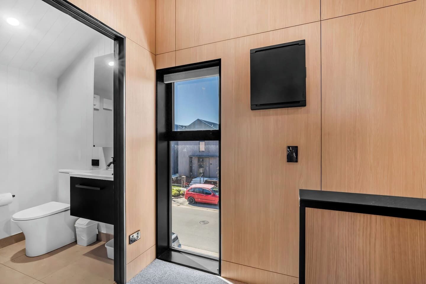 A modern bathroom with a toilet, sink, and a glass door leading outside.