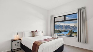 Ein Hotelzimmer mit Bett, Nachttisch, Lampe, Fenster und Bergblick, sowie einem Vorhang.