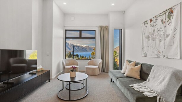 Ein modernes Wohnzimmer mit großem Fenster und Blick auf die Berge, einem Flachbildfernseher, einem runden Couchtisch und einer Couch mit Überwurfdecke.