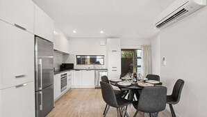 Eine moderne Küche mit Edelstahlgeräten, eine Essecke mit Tisch für vier Personen und ein Ausblick ins Freie durch ein Fenster.