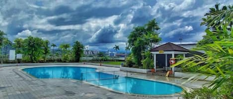 A swimming pool with a curved design, surrounded by greenery and a small pavilion.