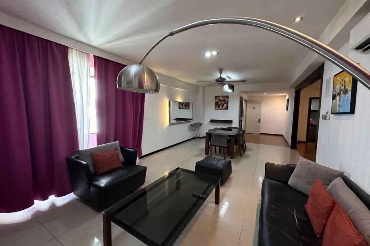 A modern living room with a glass coffee table, black leather sofa, and a dining area with a table and chairs.