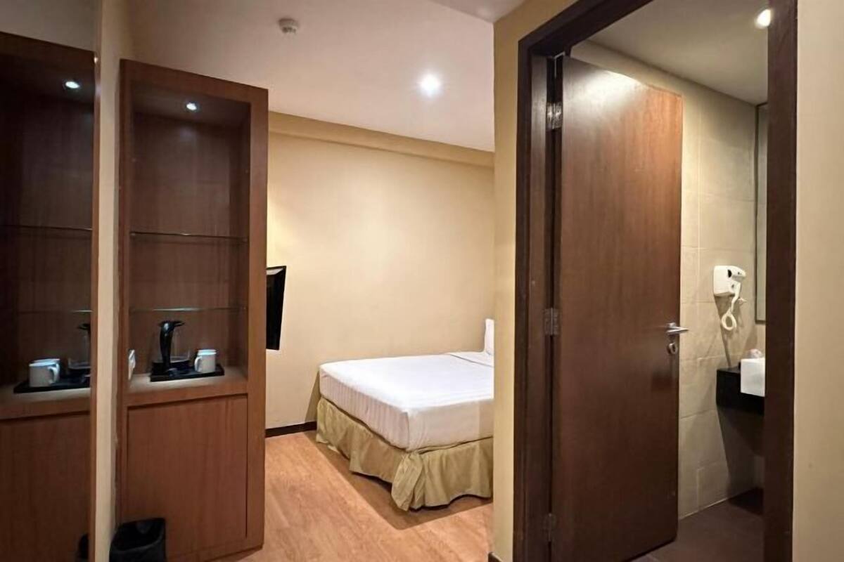 A hotel room with a bed, a small desk with a coffee maker, a wardrobe, and a bathroom with a toilet and sink.