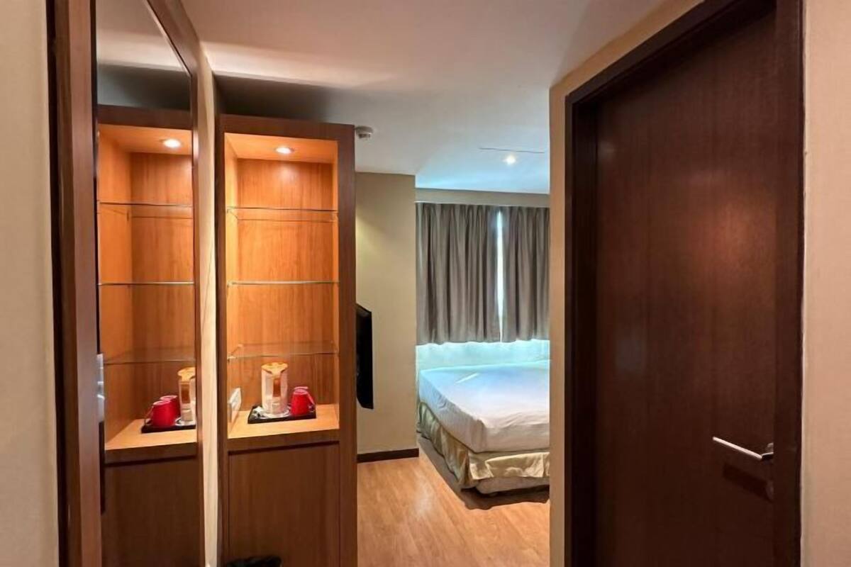 A hotel room with a wooden wardrobe, a bed, a television, and a door.