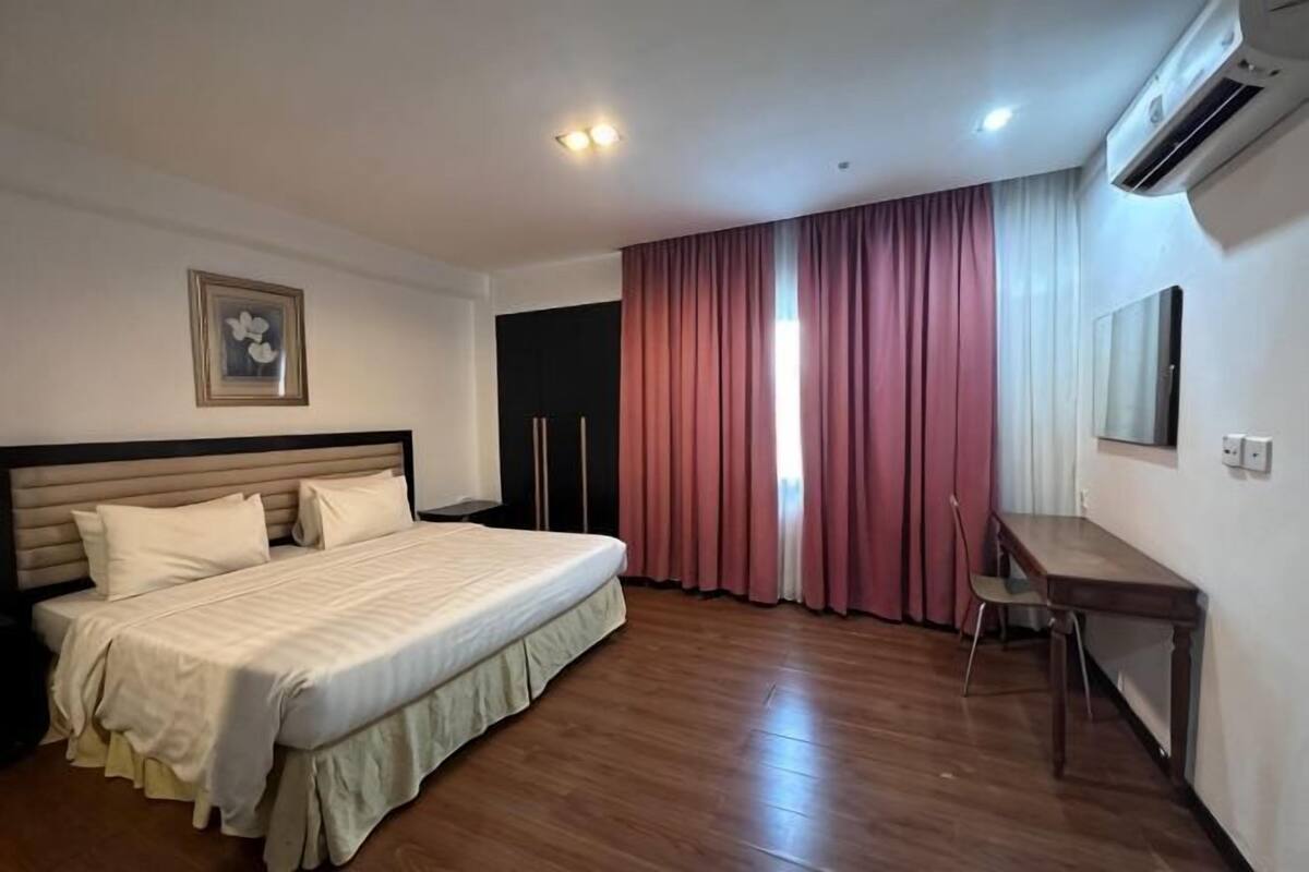 A hotel room with a bed, a desk, a chair, and a window with curtains.