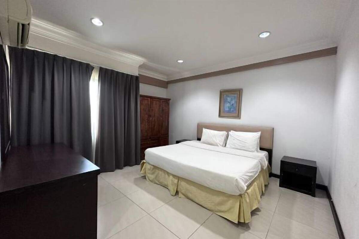 A hotel room with a bed, a desk, a wardrobe, and a painting on the wall.