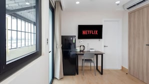 A modern hotel room with a large window, a flat-screen TV mounted on the wall, a small kitchenette, and a wooden wardrobe. - Siris Mia Residence - Self Check In (Ho Chi Minh City)