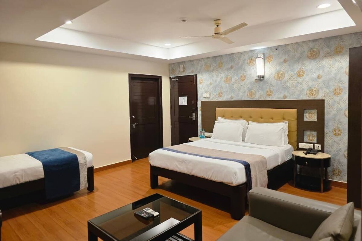 Ein Hotelzimmer mit einem großen Bett, zwei kleineren Betten, einem Schreibtisch und einem Deckenventilator.