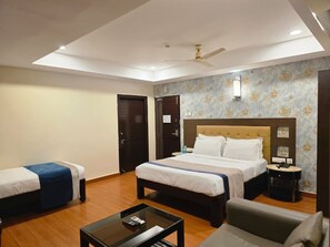 Een hotelkamer met een groot bed, twee kleinere bedden, een bureau en een plafondventilator.