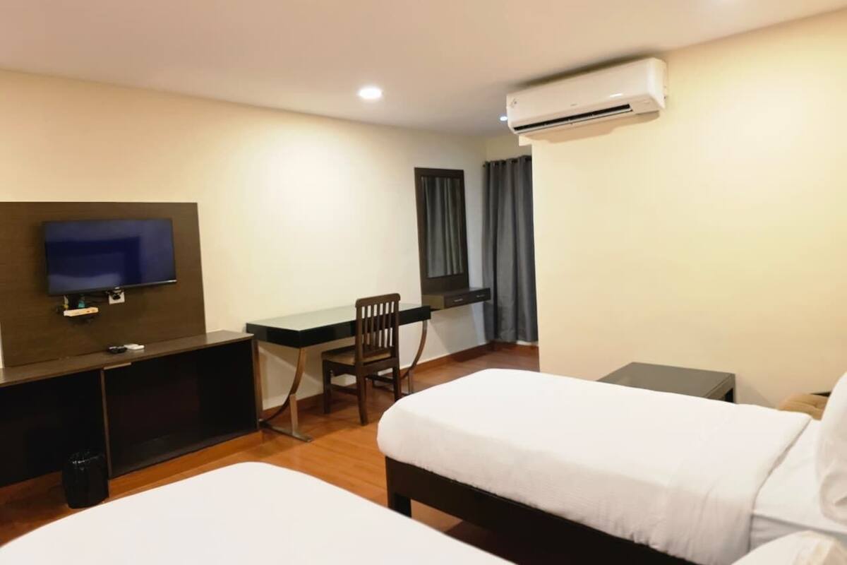 Ein Hotelzimmer mit zwei Betten, einem Schreibtisch, einem Stuhl, einem Fernseher und einer Klimaanlage.