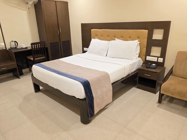 Une chambre d’hôtel bien aménagée, avec un grand lit, une table de chevet avec un téléphone, une chaise, un bureau avec une bouilloire et une armoire.