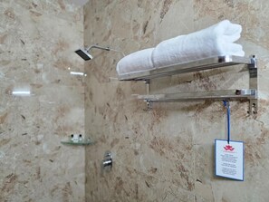 Een badkamer met een marmeren wand, een handdoekhouder met een opgevouwen handdoek, een douchekop en een bordje aan de muur.