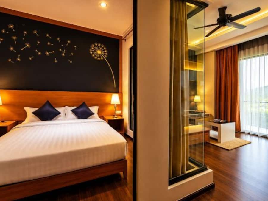 Habitación de hotel con una cama grande, lámparas de noche, ventilador de techo, un ventanal con cortinas y vistas al exterior.
