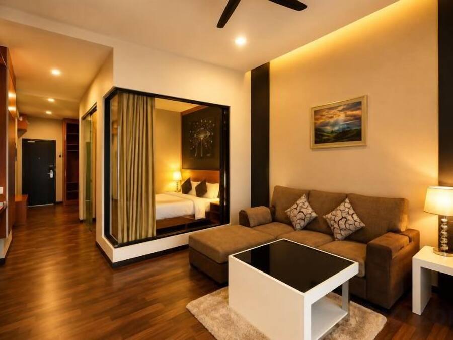 A modern hotel room with a sofa, a small table, a lamp, and a large mirror.