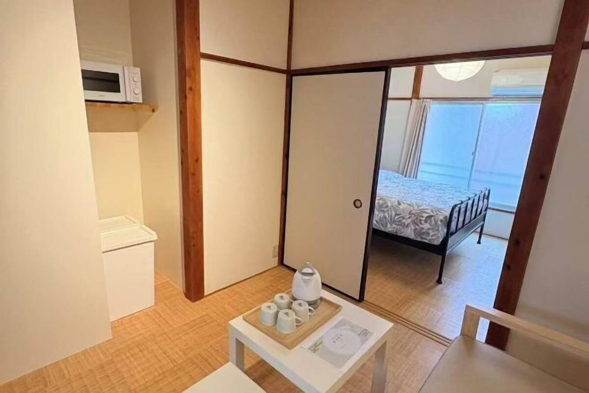 A room with a bed, a microwave, a small table with cups, and a sliding door leading to another room.