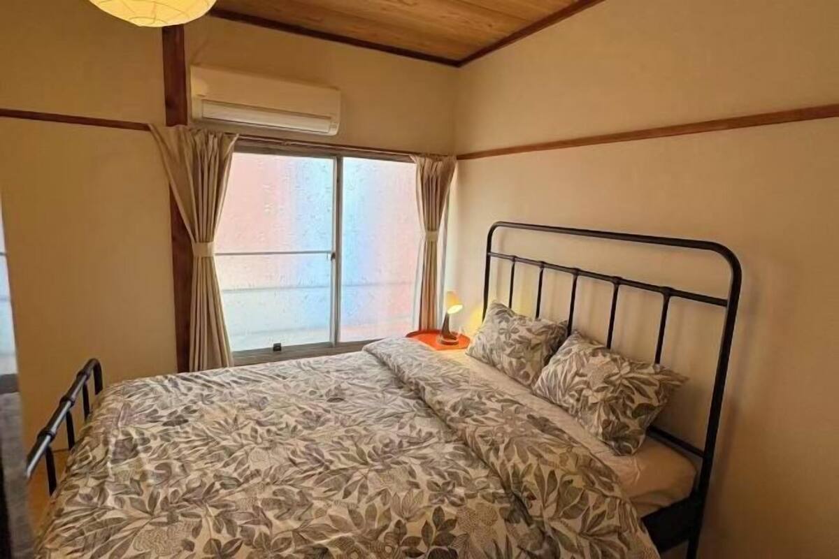 A bedroom with a bed, curtains, a window, and an air conditioning unit.