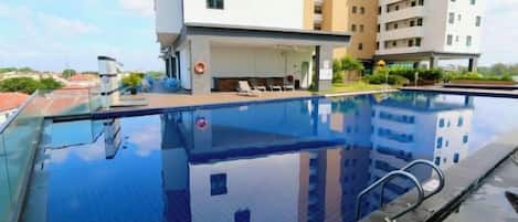 A swimming pool with a glass edge, surrounded by a building with multiple floors and balconies.