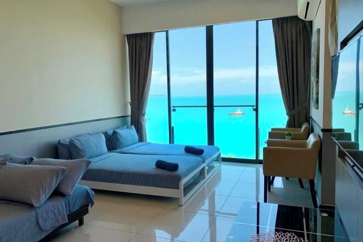 Habitació d'hotel moderna amb un llit gran, un sofà, un balcó amb vista a l'oceà i una zona de seients amb cadires.