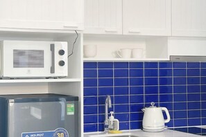 A kitchen with white cabinets, a microwave, a coffee maker, and blue-tiled backsplash.