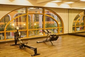A gym with exercise equipment, large windows, and a wooden floor.