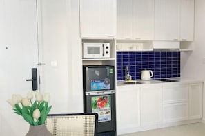 A kitchen with white cabinets, a microwave, a refrigerator, and a sink.