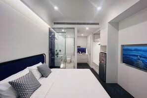 A modern hotel room with a large bed, a glass shower enclosure, and a view of the bathroom.