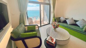 Un salon moderne avec un canapé, un fauteuil, une table basse et une vue sur l’océan depuis un balcon.